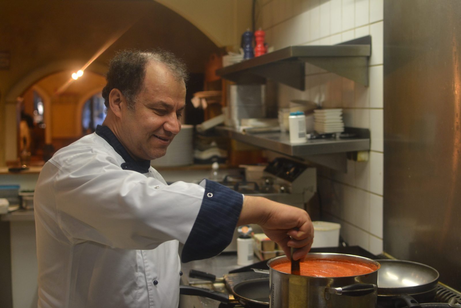 Chef-kok Emad roert in een pan tomatensaus in de keuken van Bella Roma