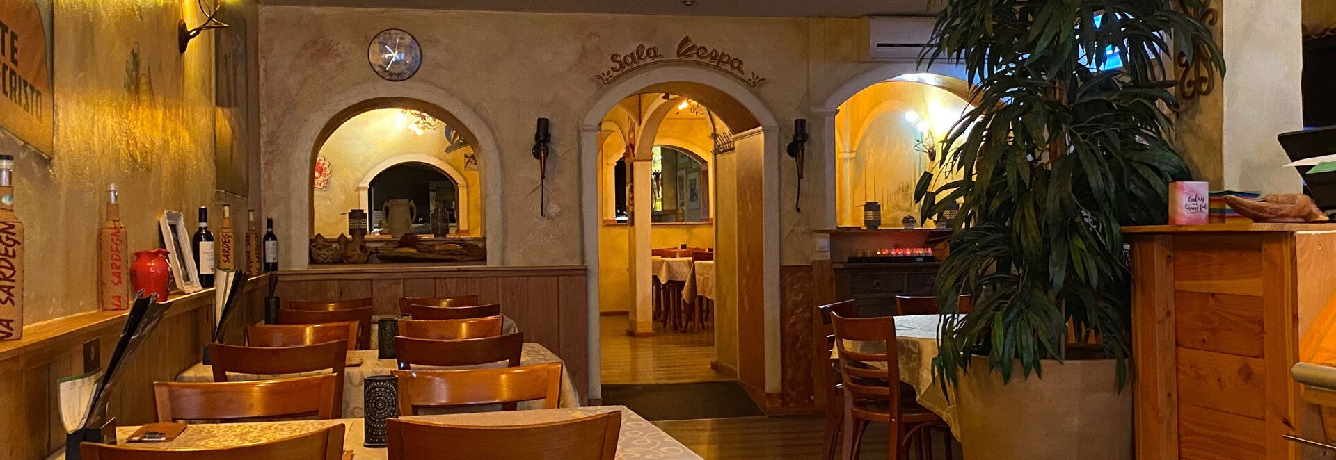 Het restaurant van Bella Roma: warme muren, houten stoelen en de boogdeuren naar de oven